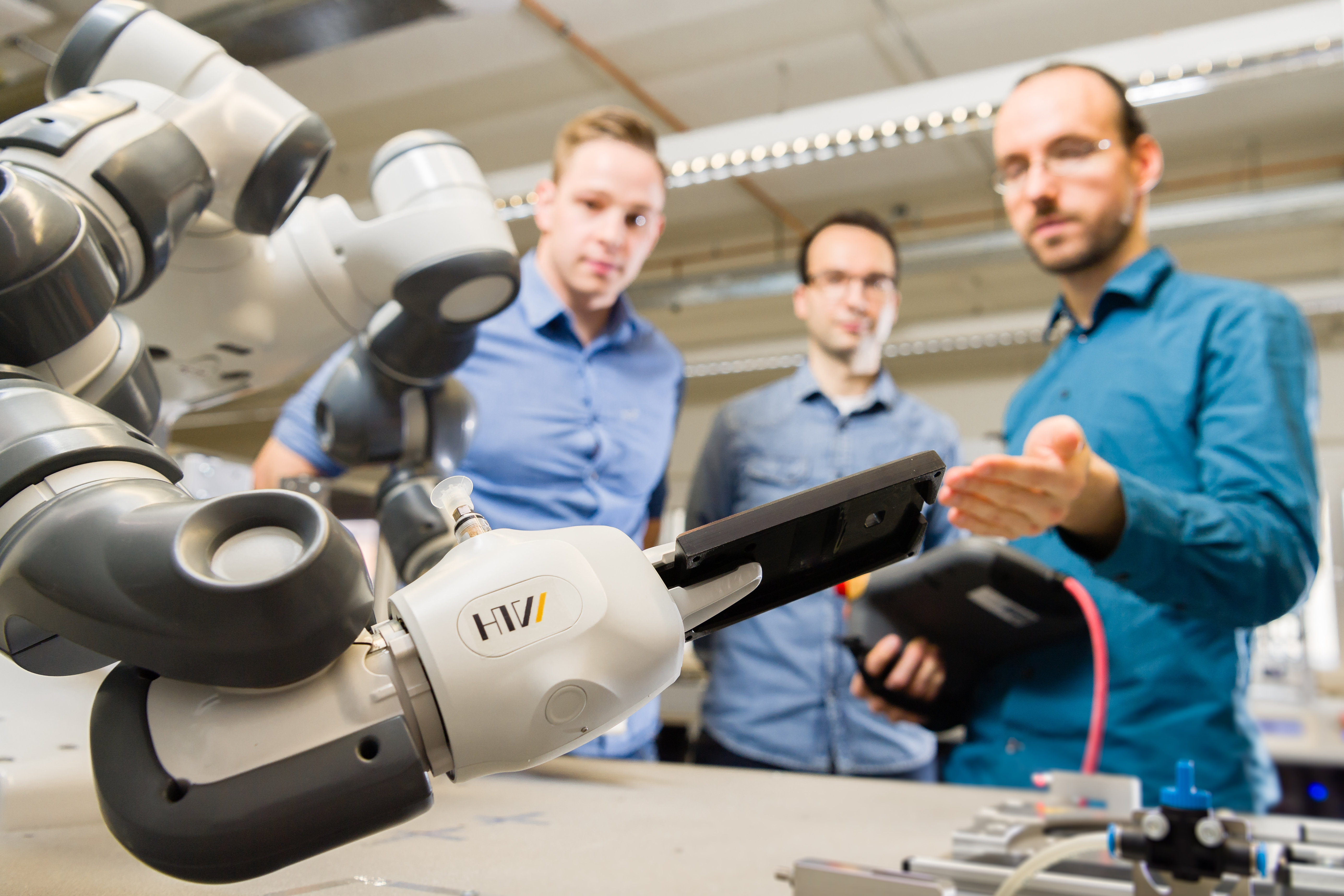 Kollaboration zwischen Mensch und Maschine praktisch erklärt Der Roboter Yumi im Vordergrund und drei Personen im Hintergrund.